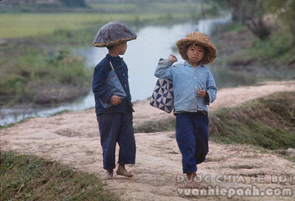 1967. Trẻ em miền Bắc chân đất đi học, đội mũ rơm chống mảnh bom.